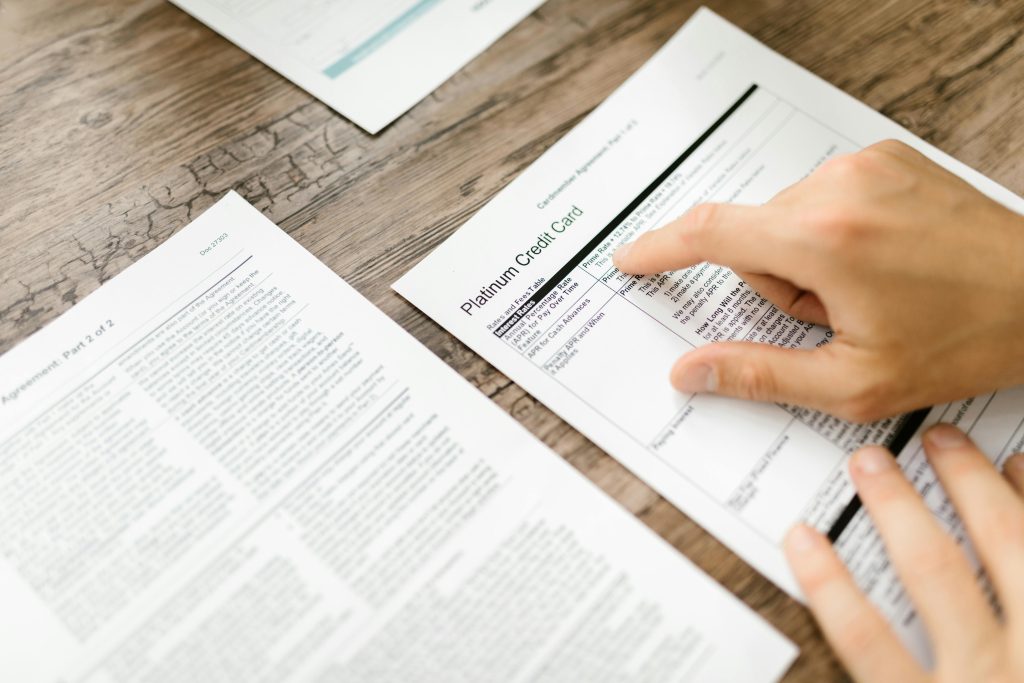 A hand examining a credit card agreement on a wooden desk, highlighting financial review.